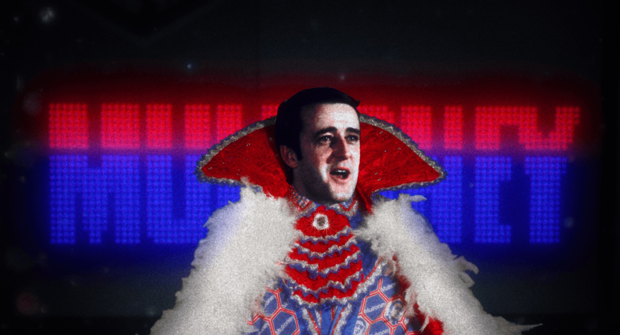 The face of a middle-aged man is superimposed atop an elaborate sequinned suit against a wall of blue and red lights.